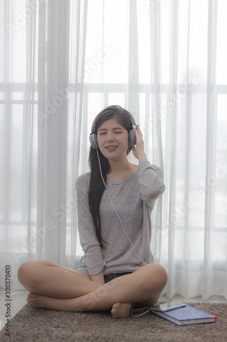 A sexy woman listening to music in the bedroom headphones with soft light by the window