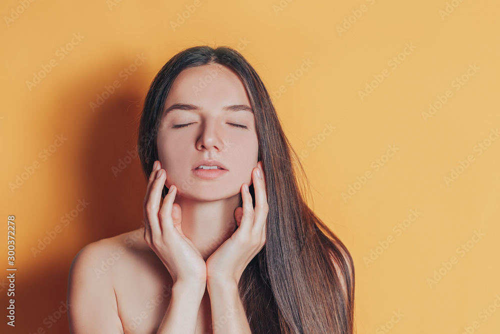 Clean face of young beautiful woman with fresh skin without cosmetics on yellow background touch her fase and closes eyes. Clean face of young beautiful woman with fresh skin without cosmetics on yellow background touch her fase and closes eyes.