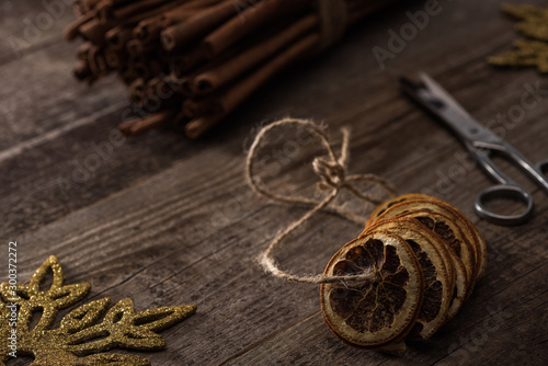 selective focus of dried citrus slices on thread near cinnamon, scissors and snowflake on wooden background