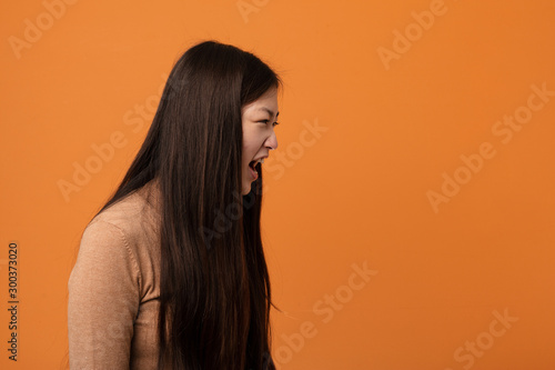 Young pretty chinese woman shouting towards a copy space