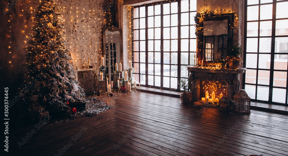 Fototapeta ciepły przytulny wieczór luksusowy wystrój wnętrza pokoju bożonarodzeniowego, choinka ozdobiona złotymi światłami prezenty prezenty, świece, girlanda lustrzana oświetlenie kominek.pokój dzienny. Koncepcja świąt noworocznych