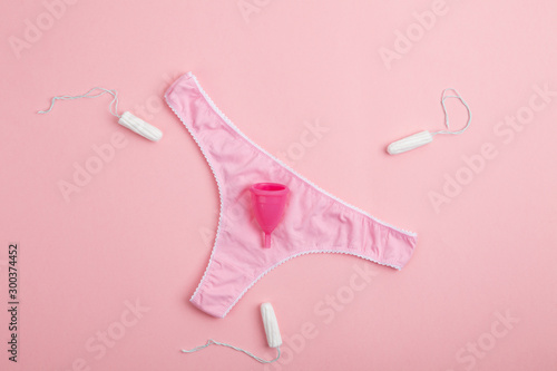 Different types of feminine hygiene products-menstrual cups, sanitary pads and tampons. Pink women's panties with sanitary napkins, tampons, menstrual cup on pink background. Concept of menstruation. 