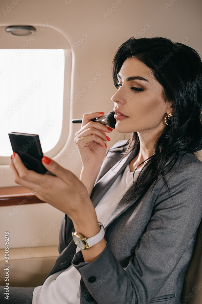 attractive businesswoman holding cosmetic brush near face in private jet attractive businesswoman holding cosmetic brush near face in private jet