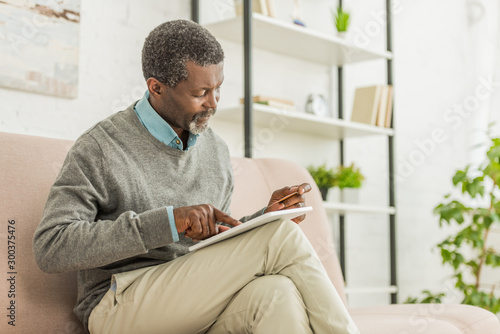 attentive african american man holding credit card while using digital tablet