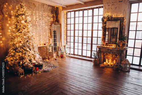 Fototapeta Naklejka Na Ścianę i Meble -  warm cozy evening luxury Christmas room interior design, Xmas tree decorated by gold lights presents gifts, candles,mirror garland lighting fireplace.holiday living room. New year holidays concept