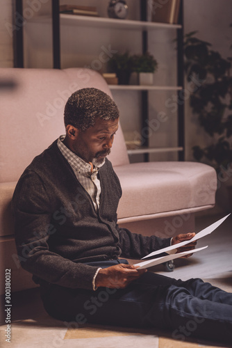 discouraged african american man sitting on floor and holding utility bills photo