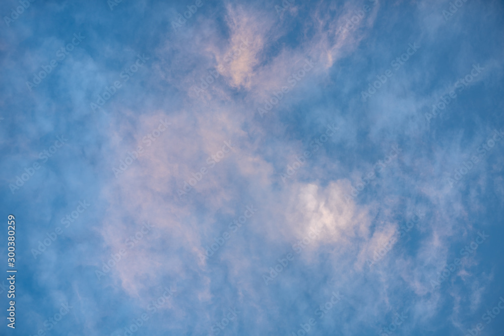 Blue sky background with clouds glowing in light pink color