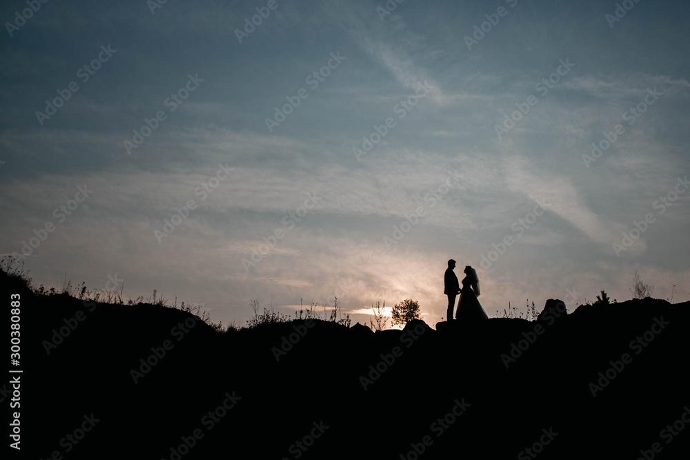 Fototapeta premium Silhouettes of a young couple lovers at sunset on dramatic sky background. Place for text or advertising