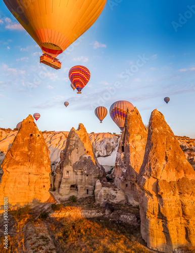 Bright yellow sunrise with colourful balloons floating just above cave homes in Cappodocia