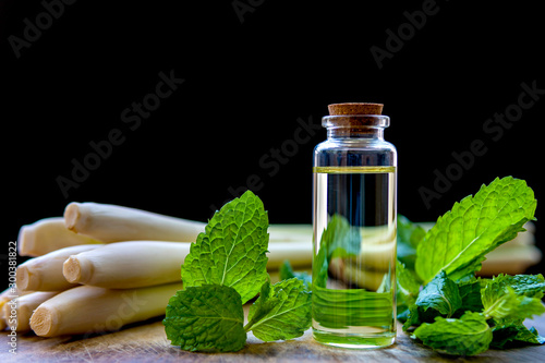 Peppermint and Lemongrass Essential oil bottle with fresh peppermint and lemongrass, placed on a wooden plate and have a black background.