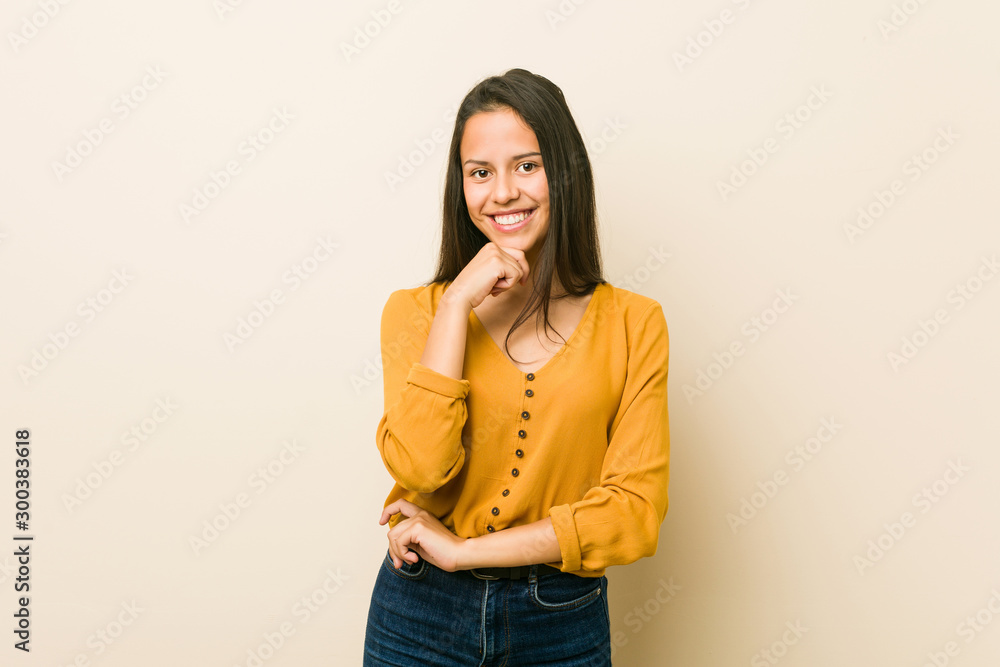 Young hispanic woman against a beige background smiling happy and confident, touching chin with hand. Young hispanic woman against a beige background smiling happy and confident, touching chin with hand.