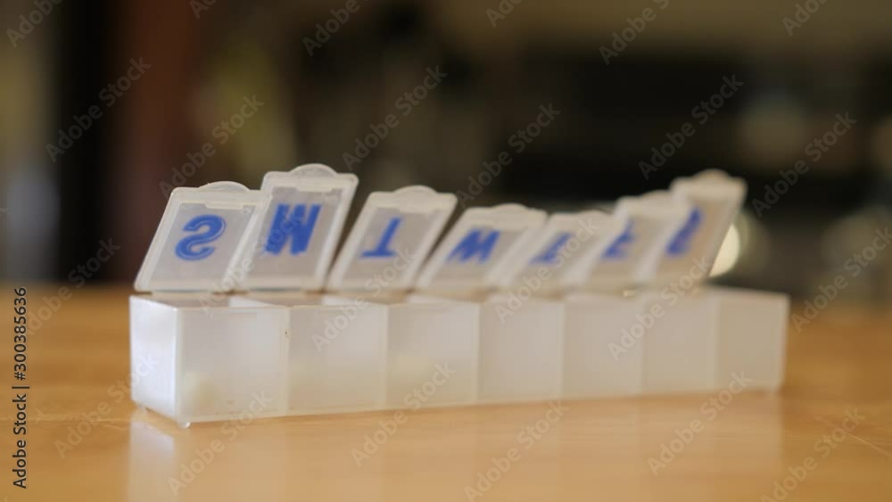 Adding supplement capsules to weekly pill box organizer. Filling pharmaceutical organizer with daily dose of medication. Adding supplement capsules to weekly pill box organizer. Filling pharmaceutical organizer with daily dose of medication.