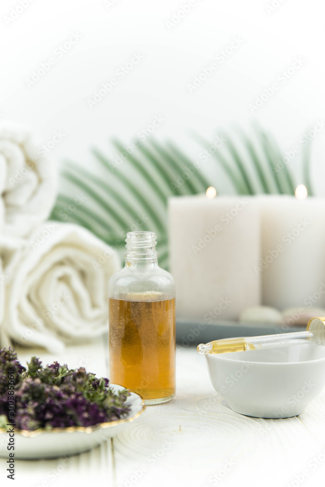 Spa treatment bottle of natural organic oil essence serum collagen. Towel, aromatic candles, flowers, massage brush and Buddha on white background. Copy space for text. Beautiful woman hands. Oil drop