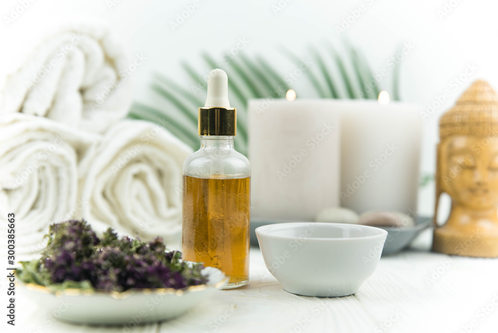 Spa treatment bottle of natural organic oil essence serum collagen. Towel, aromatic candles, flowers, massage brush and Buddha on white background. Copy space for text. Beautiful woman hands. Oil drop