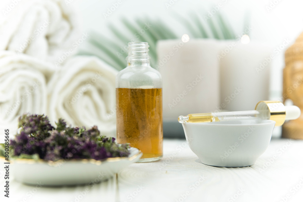 Spa treatment bottle of natural organic oil essence serum collagen. Towel, aromatic candles, flowers, massage brush and Buddha on white background. Copy space for text. Beautiful woman hands. Oil drop Spa treatment bottle of natural organic oil essence serum collagen. Towel, aromatic candles, flowers, massage brush and Buddha on white background. Copy space for text. Beautiful woman hands. Oil drop