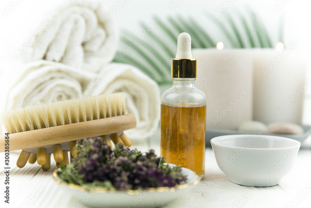 Spa treatment bottle of natural organic oil essence serum collagen. Towel, aromatic candles, flowers, massage brush and Buddha on white background. Copy space for text. Beautiful woman hands. Oil drop Spa treatment bottle of natural organic oil essence serum collagen. Towel, aromatic candles, flowers, massage brush and Buddha on white background. Copy space for text. Beautiful woman hands. Oil drop