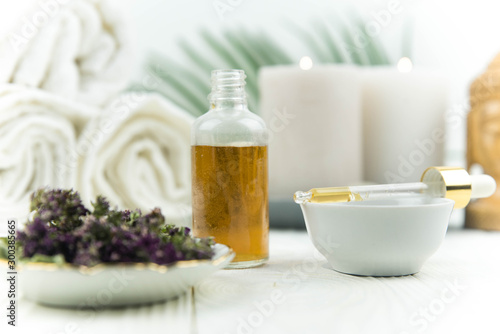 Spa treatment bottle of natural organic oil essence serum collagen. Towel  aromatic candles  flowers  massage brush and Buddha on white background. Copy space for text. Beautiful woman hands. Oil drop
