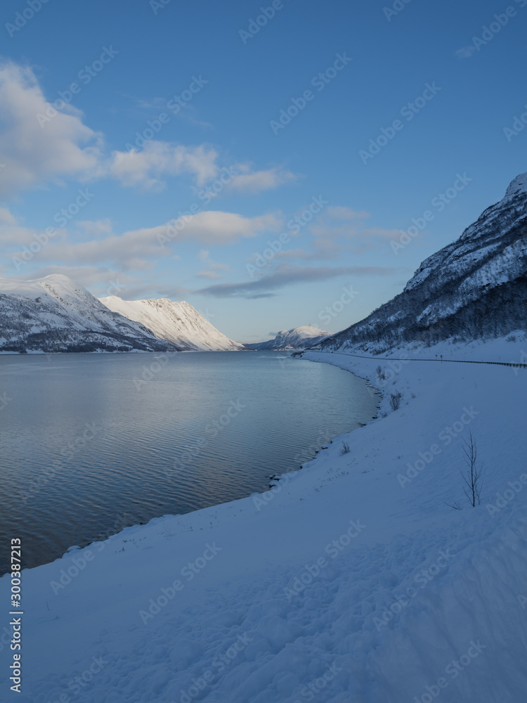 snowy mountains on the shore of the sea with a road and a blue sky in northern Norway in winter