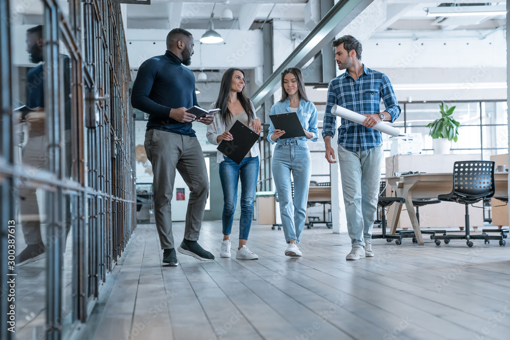 Obraz premium On the way to business meeting. Full length of young modern people in smart casual wear having a discussion while walking through the office