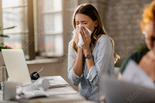 Young businesswoman using a tissue while sneezing in the office.