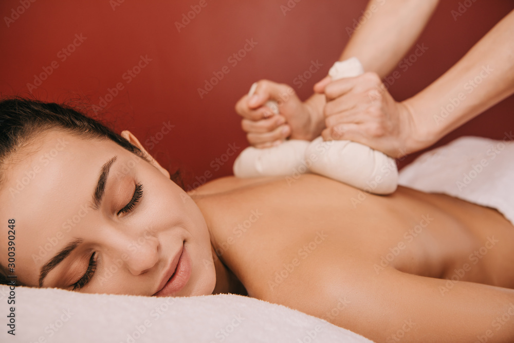 cropped view of masseur doing back massage with herbal balls to woman in spa cropped view of masseur doing back massage with herbal balls to woman in spa