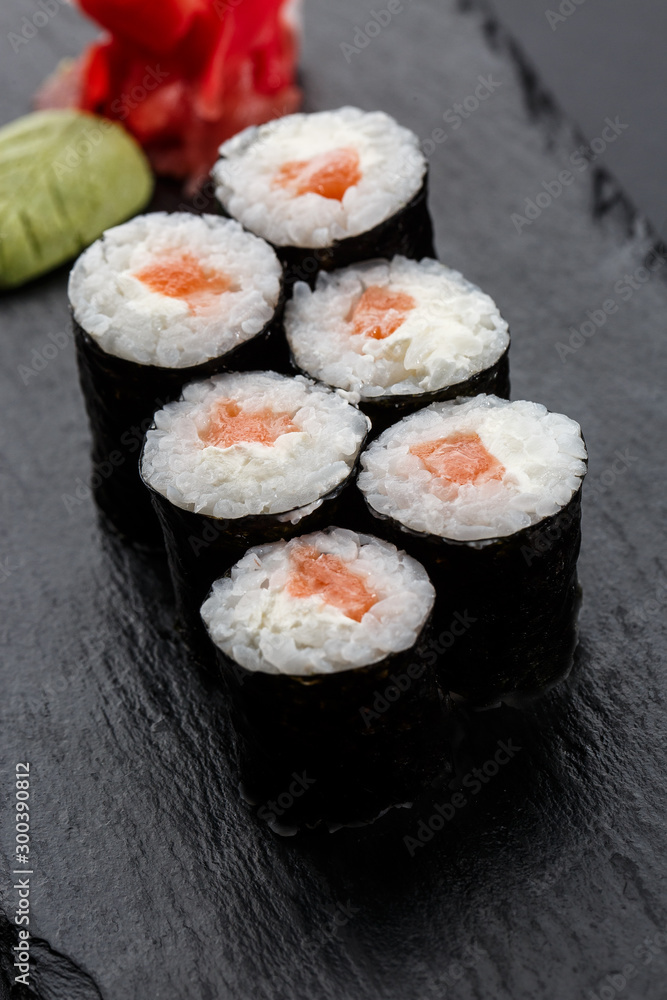 Maki Sushi Rolls with salmon on black stone on dark background. Sushi menu. Japanese food. Closeup of delicious japanese food with sushi roll. Vertical photo Maki Sushi Rolls with salmon on black stone on dark background. Sushi menu. Japanese food. Closeup of delicious japanese food with sushi roll. Vertical photo