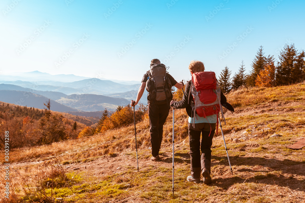 Two old people with large backpacks hike through the autumn mountains, the concept of active recreation in old age