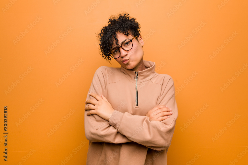 Young mixed african american woman against a brown background frowning face in displeasure, keeps arms folded. Young mixed african american woman against a brown background frowning face in displeasure, keeps arms folded.