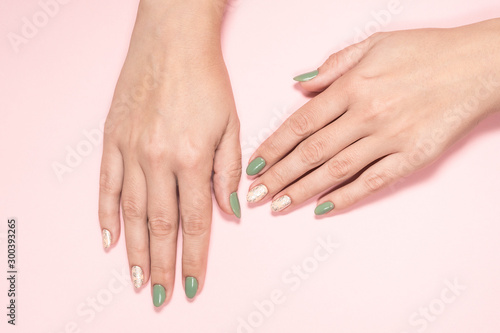 Closeup top view of beautiful two faded colors trendy manicure of green and pink nails with glossy silver stamp design isolated on pastel pink background. Winter or autumn style of nail design concept
