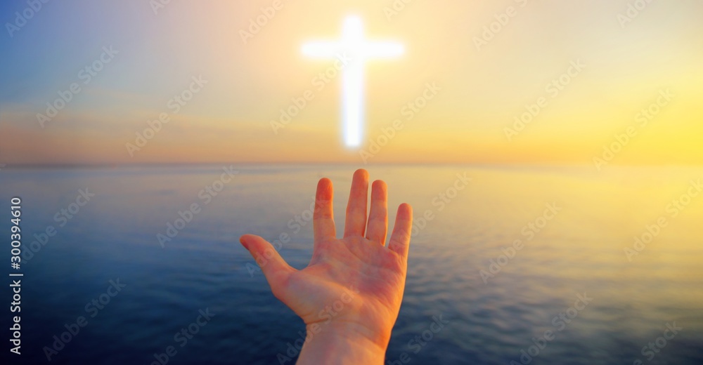 Human hand open palm pray to Christian cross light above sunset water. Jesus Christ church faith worship, god prayer hope, catholic bible religion respect, spiritual awakening soul concept background