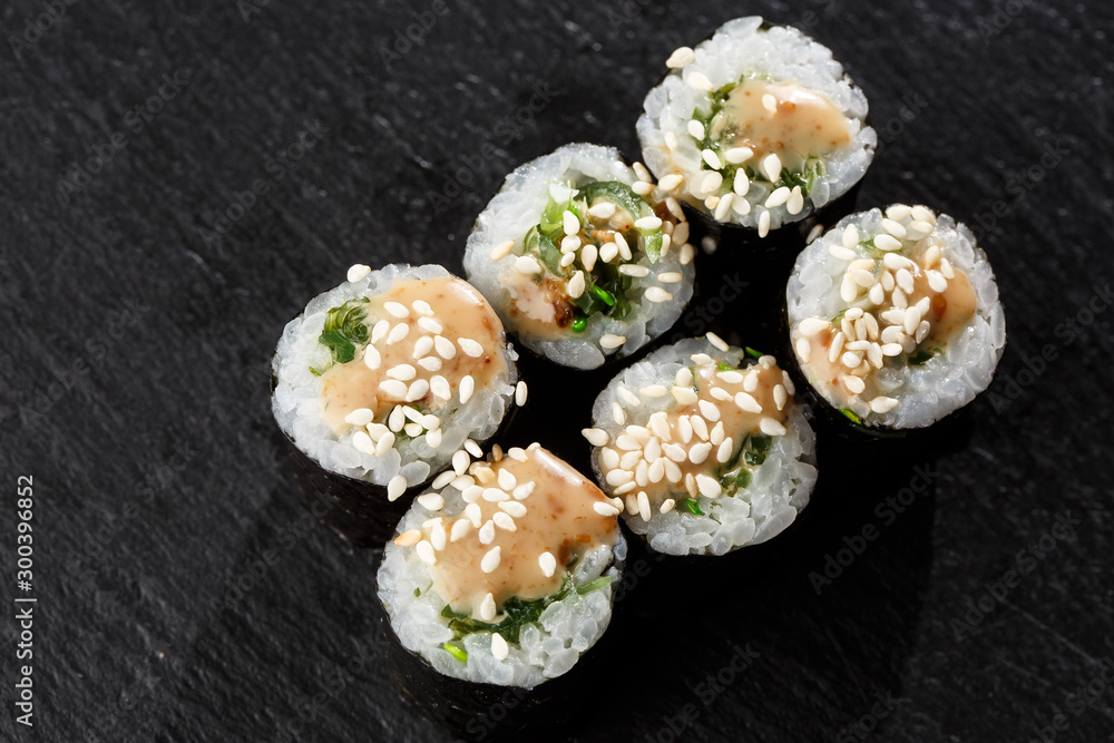 Maki Sushi Rolls with wakame and nut sauce on black stone on dark background. Sushi menu. Japanese food. Closeup of delicious japanese food with sushi roll. Horizontal photo Maki Sushi Rolls with wakame and nut sauce on black stone on dark background. Sushi menu. Japanese food. Closeup of delicious japanese food with sushi roll. Horizontal photo