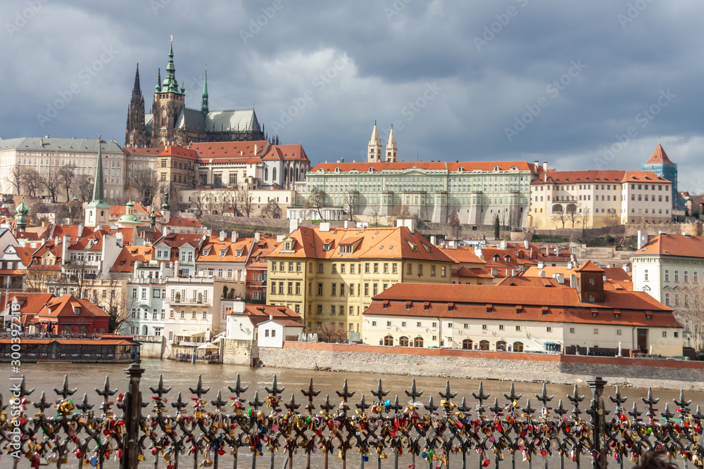 Obraz premium panoramic ancient cityscape Prague with Vltava river and famous Castle and love locks fence overcast background, Czech Republic