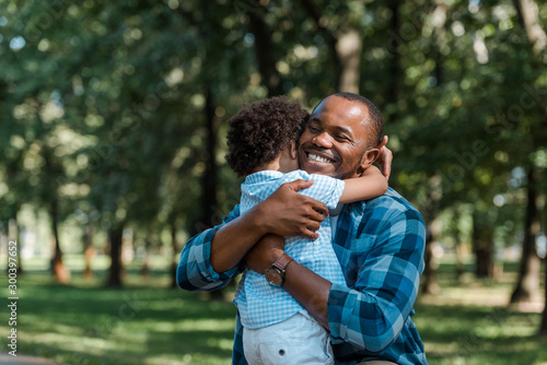 happy african american father with closed eyes hugging curly son photo