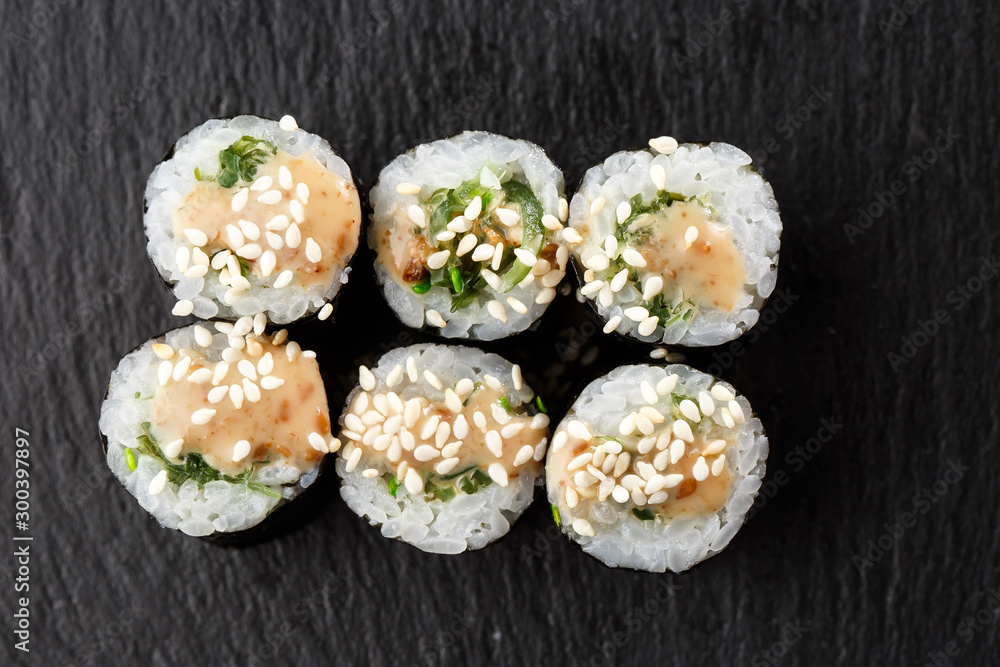 Maki Sushi Rolls with wakame and nut sauce on black stone on dark background. Sushi menu. Japanese food. Closeup of delicious japanese food with sushi roll. Horizontal photo Maki Sushi Rolls with wakame and nut sauce on black stone on dark background. Sushi menu. Japanese food. Closeup of delicious japanese food with sushi roll. Horizontal photo