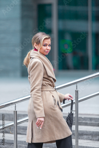 Outdoors lifestyle fashion portrait of stunning brunette girl. Walking on the city street. Going shopping. Wearing stylish white fitted coat, red neckscarf, black umbrella cane. Business woman.