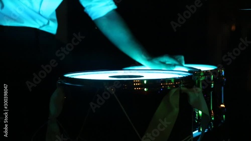 The drummer plays with sticks an average tempo on light drums. It's dark around photo