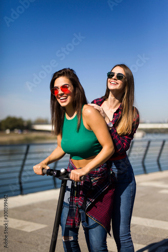 Pretty young female friends riding an electric scooter in the street © BGStock72