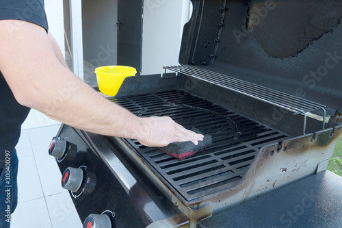 The male hand cleans the black grill with a soft brush. Grill for frying meat. Cleaning the outdoor gas grill.