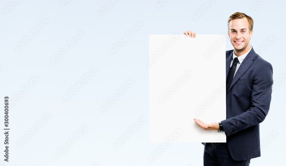 Happy confident successful businessman showing blank board, isolated against grey background. Empty copy space for some slogan or advertising sign text. Happy confident successful businessman showing blank board, isolated against grey background. Empty copy space for some slogan or advertising sign text.