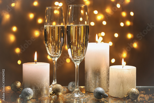 Champagne glasses, candles and baubles against blurred lights background, space for text
