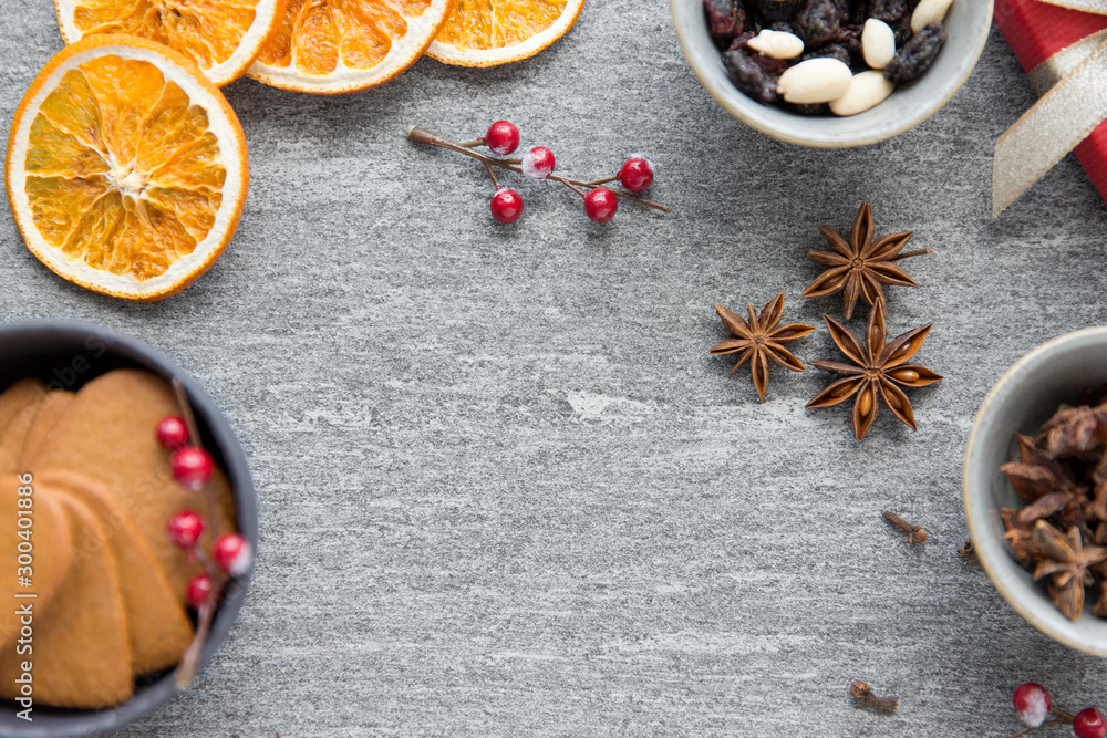 Fototapeta premium christmas, winter holidays and seasonal drinks concept - hot mulled wine, dry orange slices, raisins with pine cones and aromatic spices on grey background