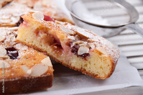 A piece of plum pie with almond petals and icing sugar