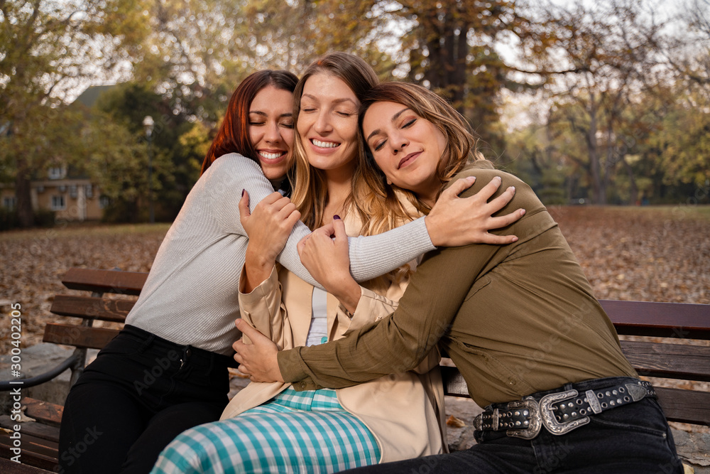 Affectionate female friends hugging while sitting on the bench, eyes closed Affectionate female friends hugging while sitting on the bench, eyes closed