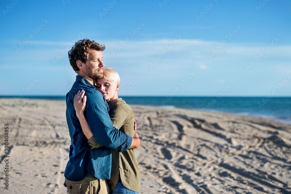 Young couple standing outdoors on beach, hugging. Copy space.