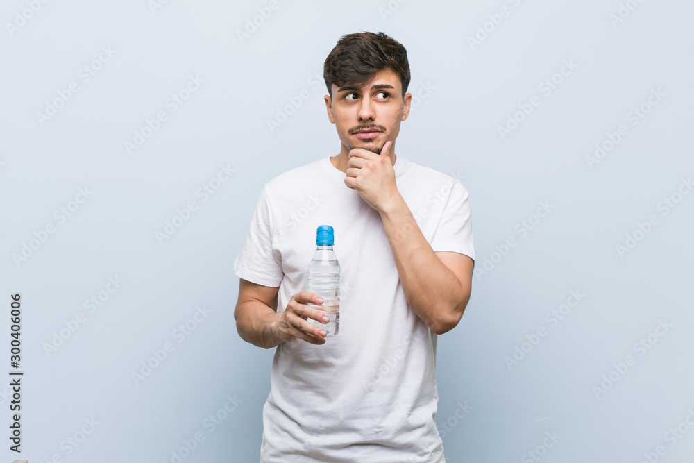 Young hispanic man holding a water bottle looking sideways with doubtful and skeptical expression. Young hispanic man holding a water bottle looking sideways with doubtful and skeptical expression.