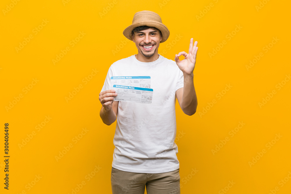 Young hispanic man holding an air tickets cheerful and confident showing ok gesture.