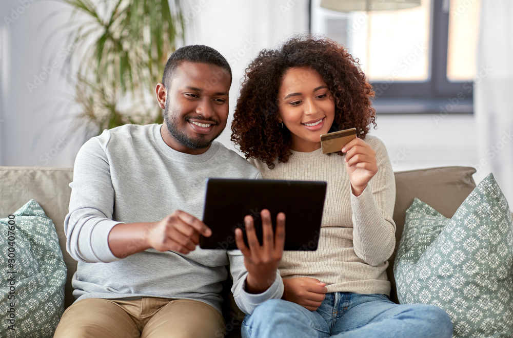 family, technology, online shopping and people concept - happy african american couple couple with tablet pc computer and credit card at home