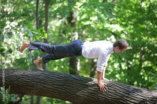 caucasian male in formal clothes, doing plank exercise - yoga asana on tree trunk