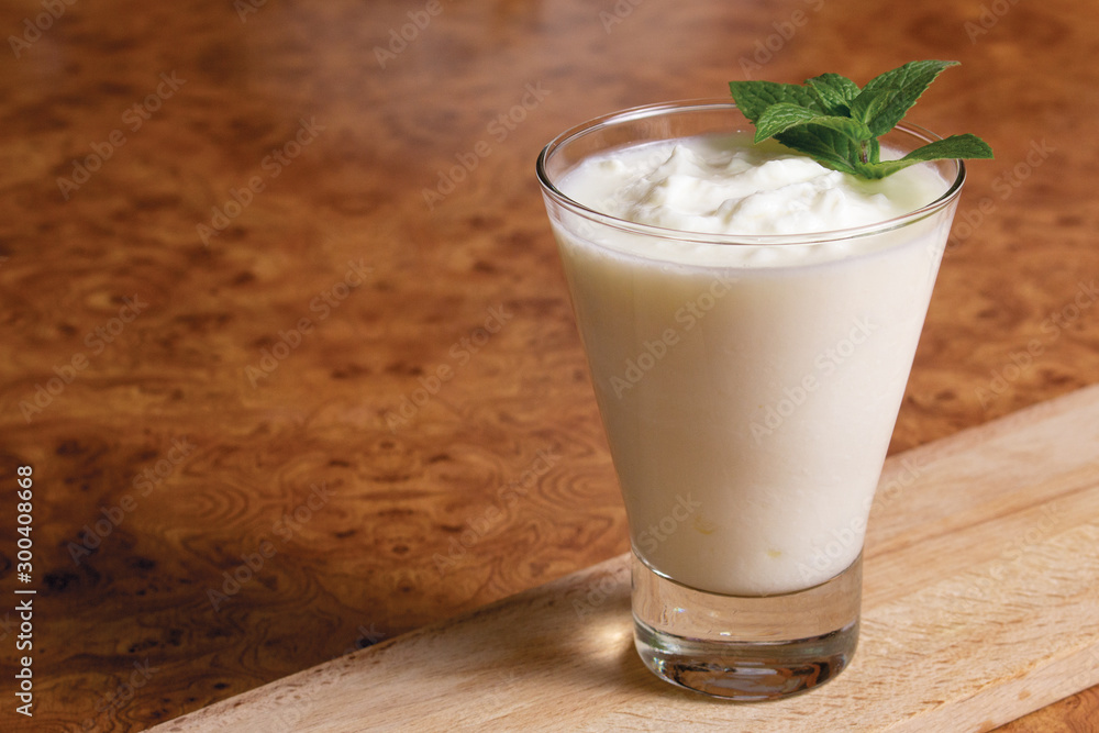 Kefir in a glass goblet with a mint branch on a wooden board on a brown background Kefir in a glass goblet with a mint branch on a wooden board on a brown background