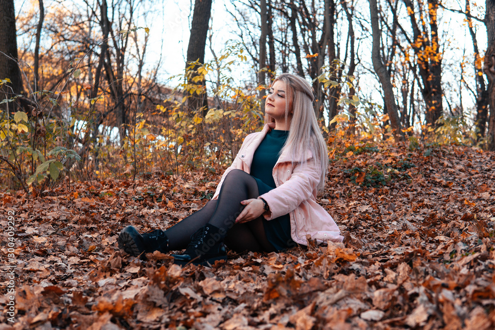 A young pleasant woman in casual clothes with long hair is sitting in the autumn forest. A young pleasant woman in casual clothes with long hair is sitting in the autumn forest.